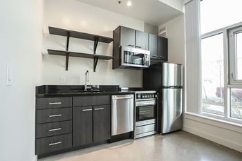A modern kitchen with stainless steel appliances and black countertops. at RiDE at RiNo Apartments, Denver 80216